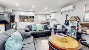 A modern living room with a sectional sofa, a coffee table, and a dining area with a kitchen in the background. - 3BR Dog-friendly Home Near River w/ Fire Pit (Bethel Island)