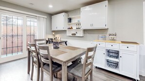 A dining area with a wooden table and chairs, white cabinets, and a window with a view of a fence. - 3BR Dog-friendly Home Near River w/ Fire Pit (Bethel Island)