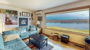 Un salon avec une grande fenêtre, un canapé, une table basse et une vue sur un lac.