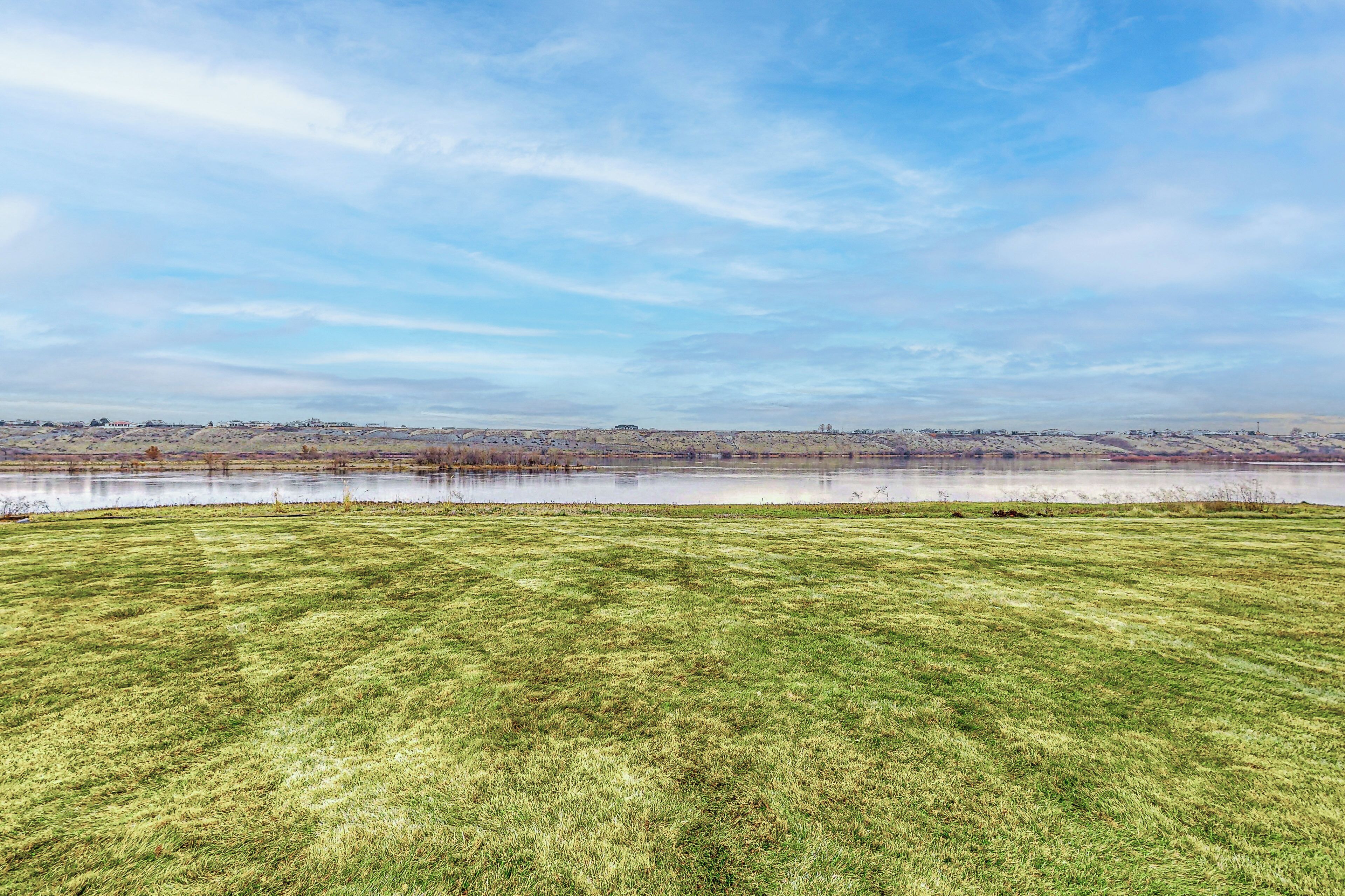 A grassy field with a body of water and distant buildings.