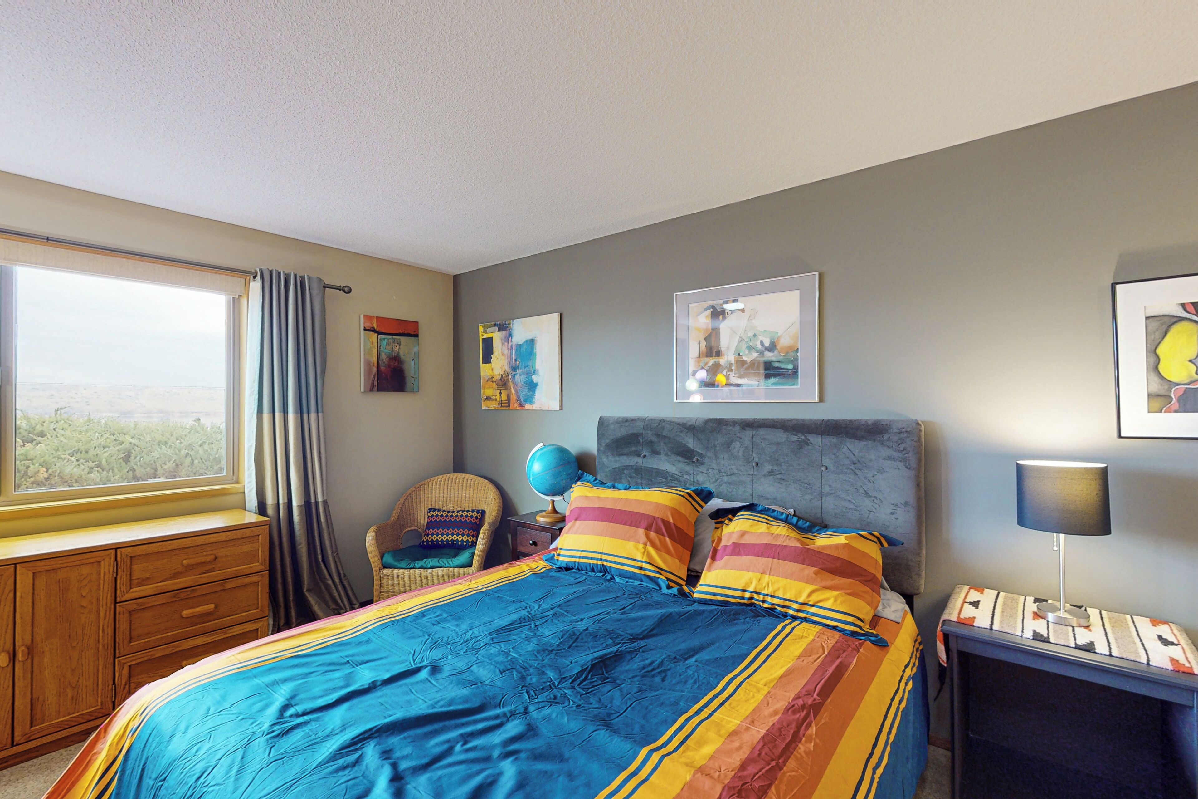 A bedroom with a large bed, a window with curtains, a globe on a nightstand, and artwork on the walls.