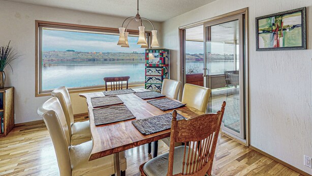 Un espace repas avec une table en bois, des chaises et une vue sur un lac, visible à travers de grandes fenêtres.