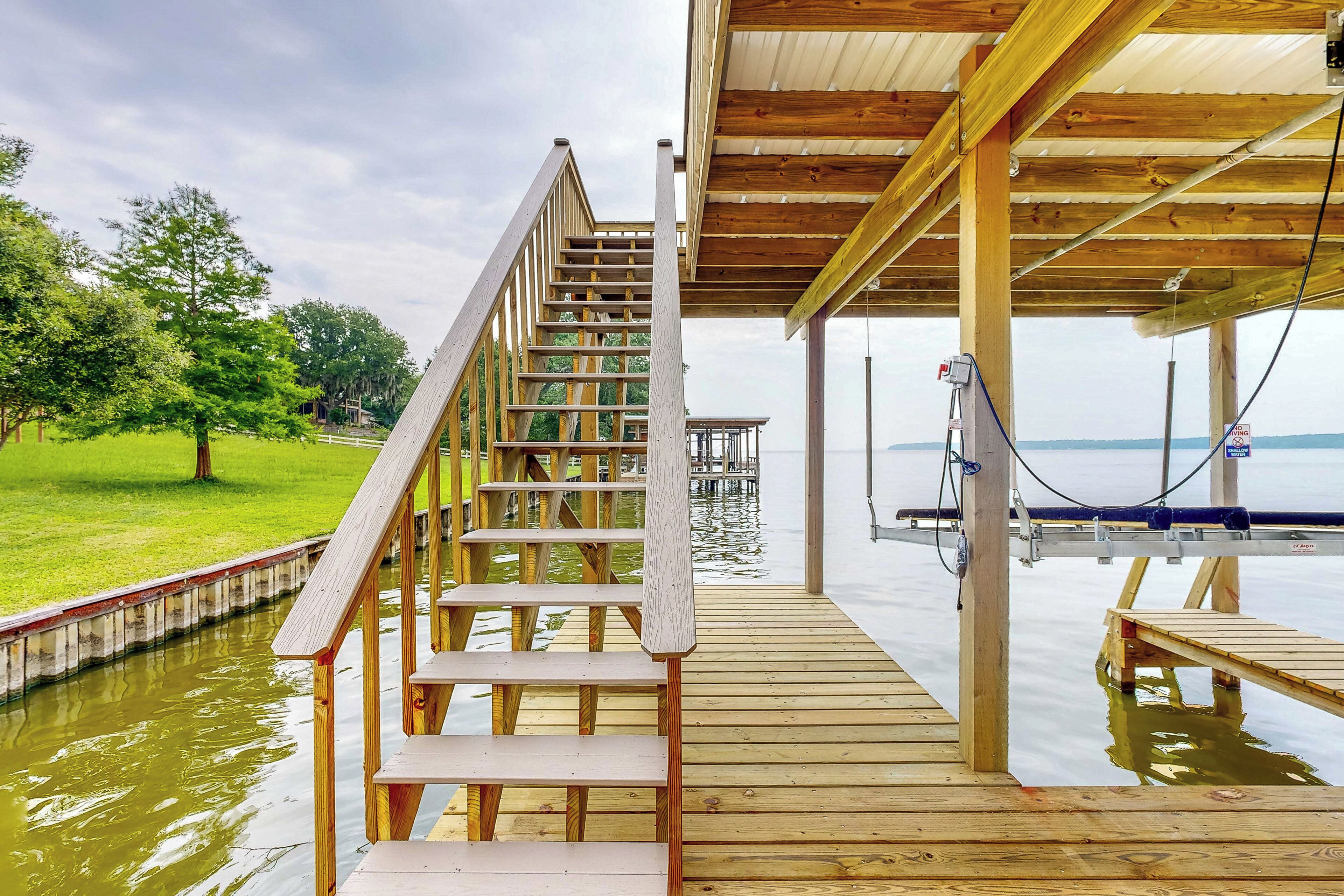 A wooden staircase leading to a covered deck over water, with a view of the water and trees in the background.