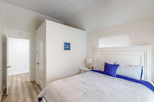 Quarto com cama, mesa de cabeceira, luminária na parede e uma porta.