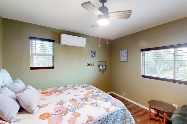 A bedroom with a bed, a ceiling fan, two windows, and a small table. - Countryside Charmer w/ Fire Pit in Washington! (Washington)