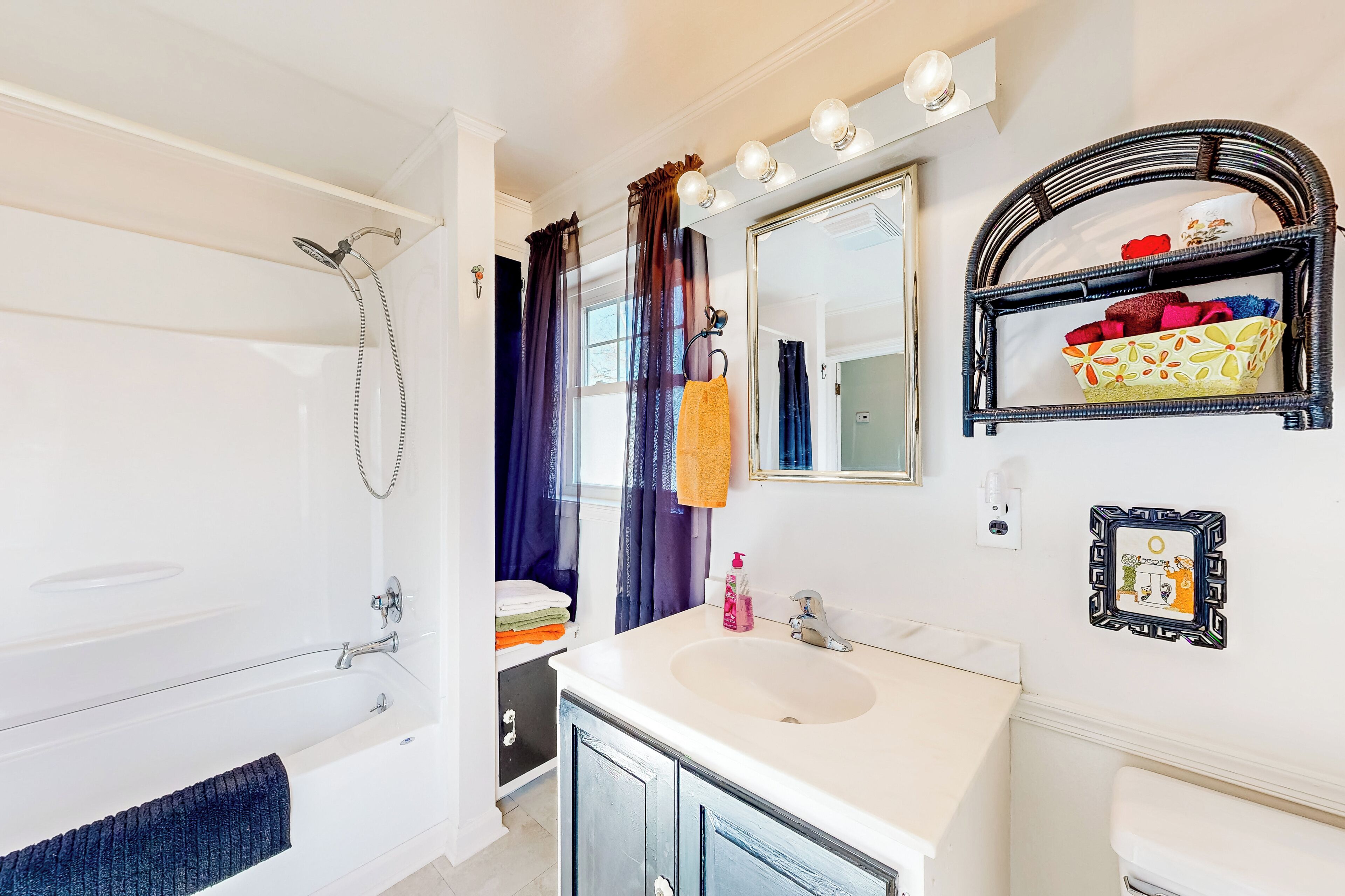 A bathroom with a bathtub, a sink, a mirror, and a shelf with towels.