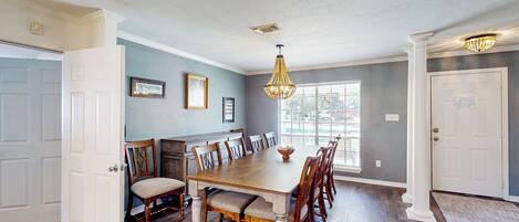 Comedor con mesa y sillas de madera, una araña y vista al exterior.