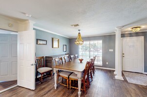 Comedor con mesa y sillas de madera, una araña y vista al exterior.