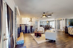 A spacious living room with a large ceiling fan, a dining area with a kitchen in the background, and a cozy seating area with a patterned rug. - Poolside Bliss! Christian Pass Family Home w/ Yard (Pass Christian)