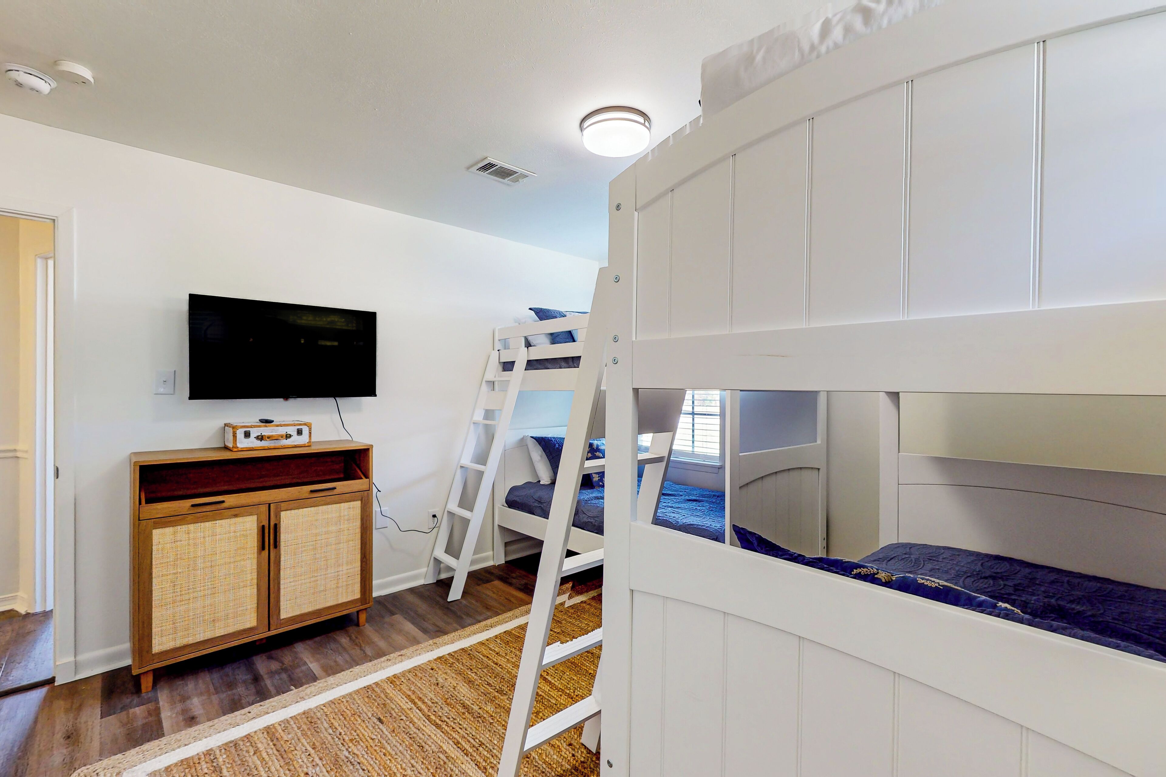 A bunk bed room with a television on the wall, a wooden cabinet, and a ladder.