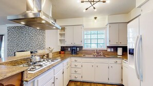 A modern kitchen with white cabinets, a granite countertop, a stainless steel range hood, and a window providing natural light. - Poolside Bliss! Christian Pass Family Home w/ Yard (Pass Christian)