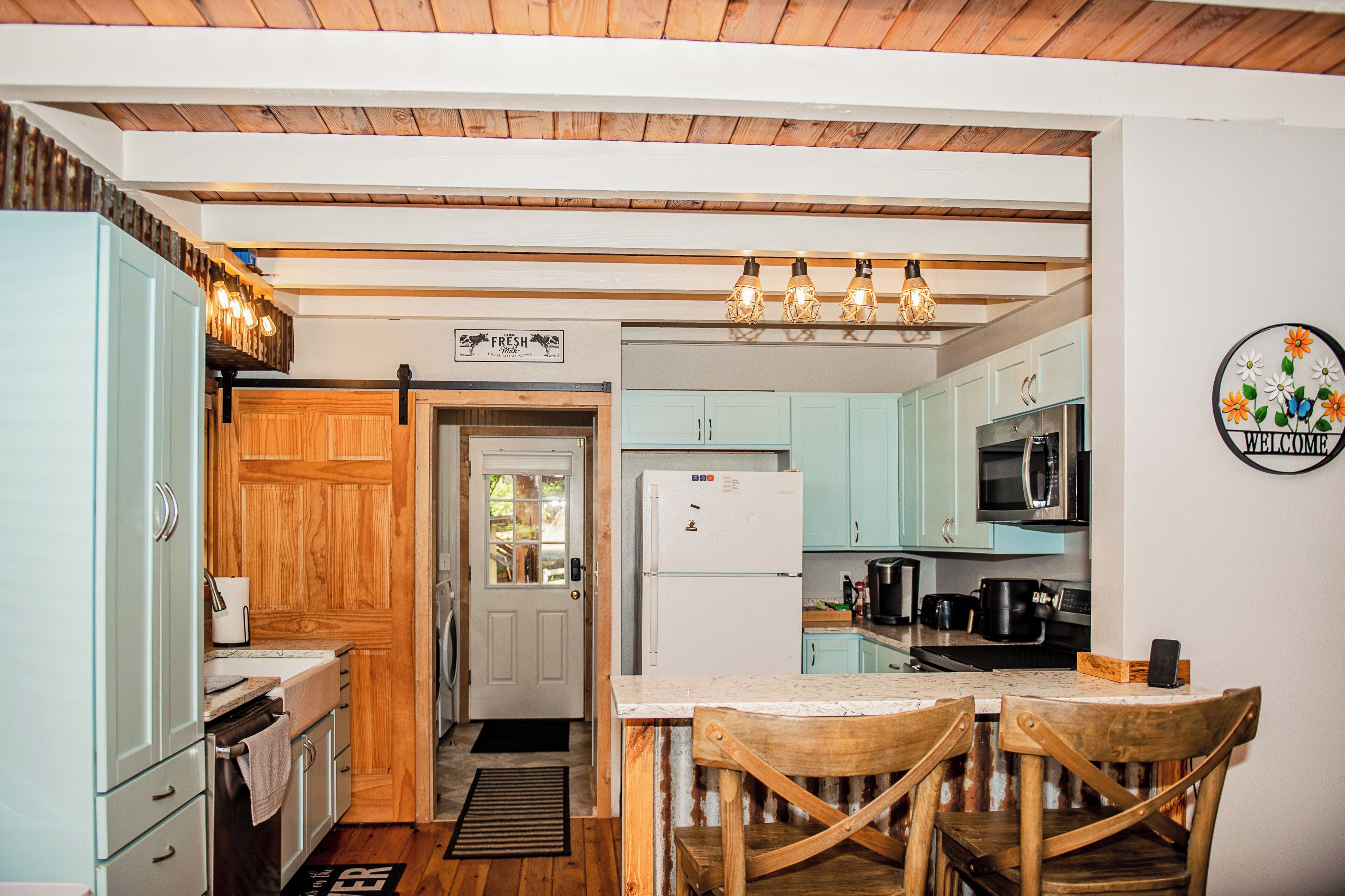 A kitchen with wooden cabinets, a refrigerator, a microwave, and a dining area with two wooden chairs.