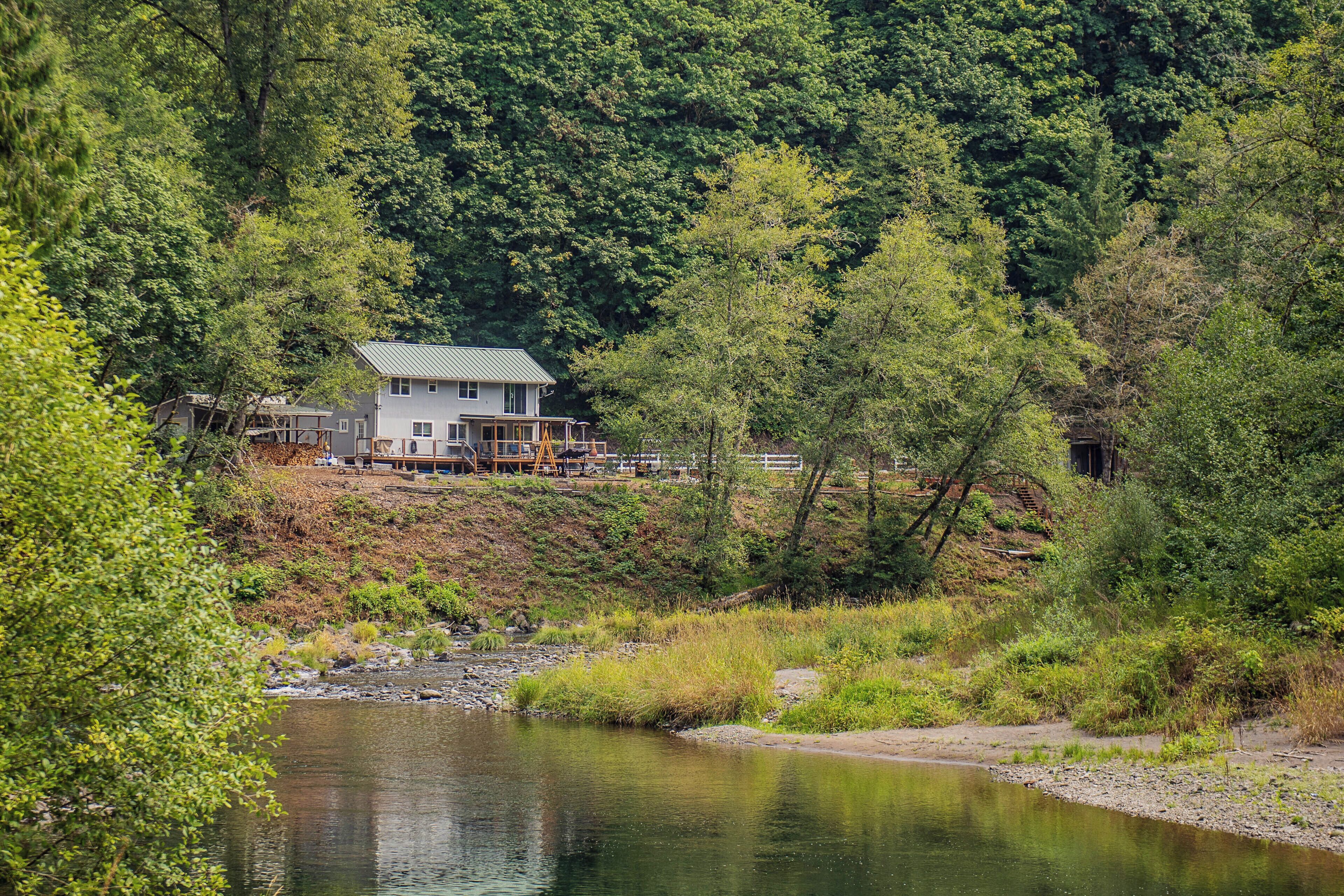 A house with a green roof, surrounded by dense forest and a calm river.