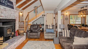 Un salón acogedor con chimenea, sillones de cuero, sofá y una escalera que lleva a un nivel superior.