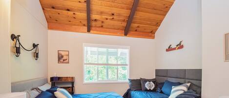 A bedroom with two beds, wooden ceiling beams, a window, and wall-mounted lights.