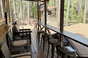 A wooden deck with wicker chairs and stools, overlooking a forested area with a cabin in the background. - Fire Pit! A-frame Escape, 33 Mi to Sunrise Park (Pinetop)