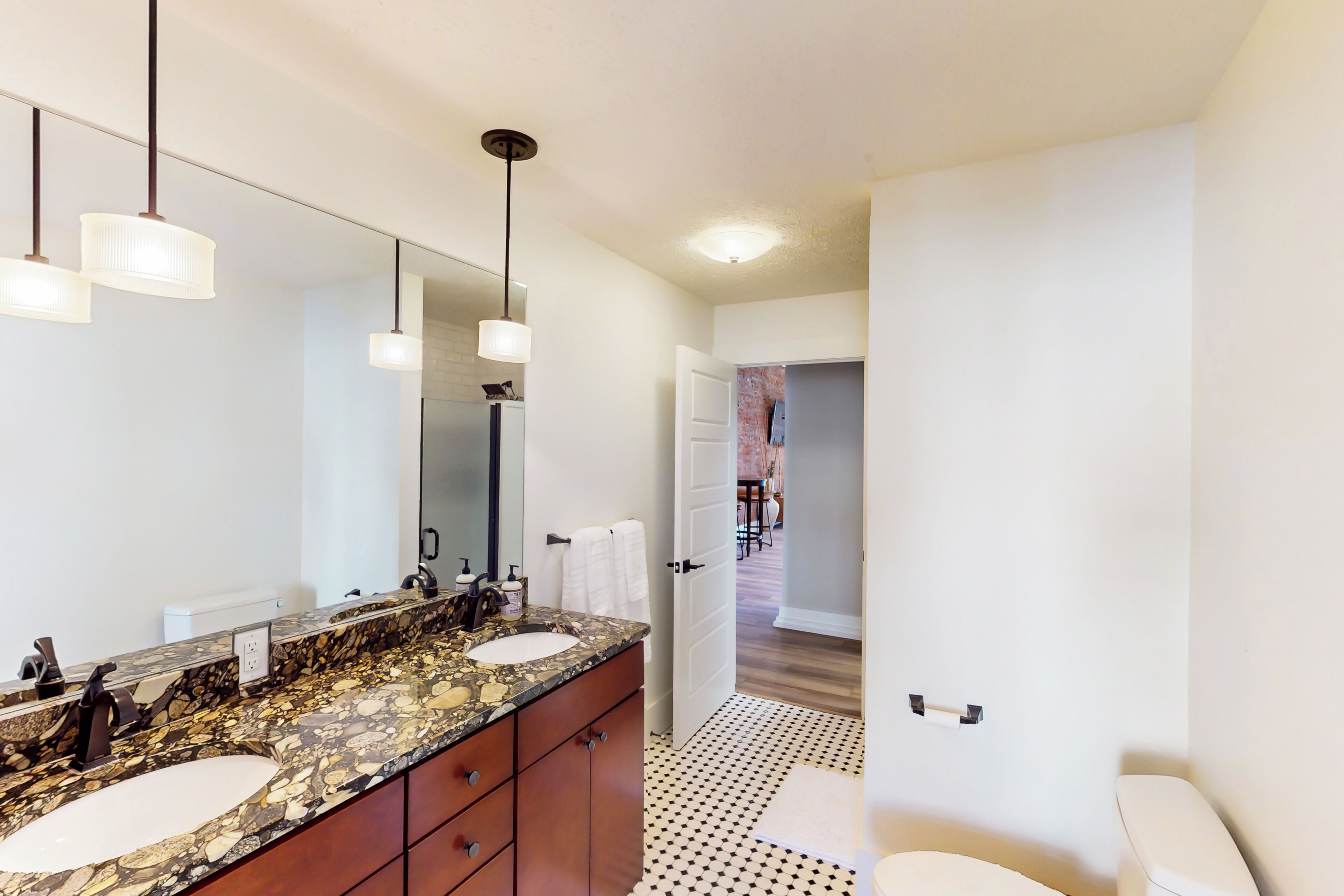 Un baño moderno con lavamanos de mármol, un espejo grande y un inodoro.