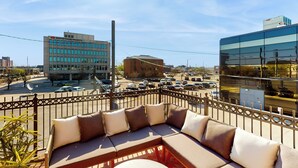 A modern outdoor seating area with a metal fence and a view of a cityscape including a building with a sign. - 'downtown Delight' w/ Patio! 1 Mi to Ball State (Muncie)