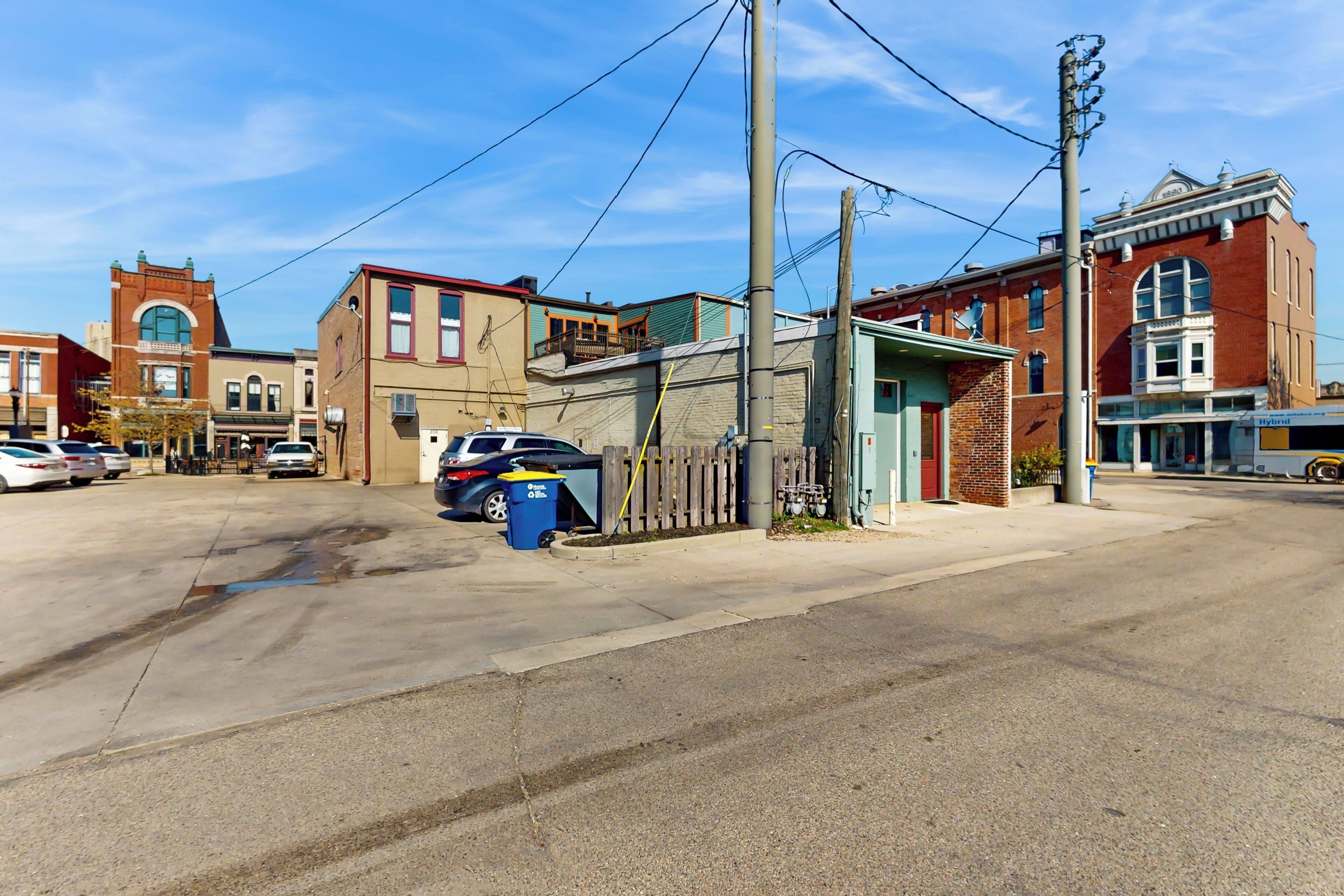 A street view with buildings, parked cars, and a visible trash bin.