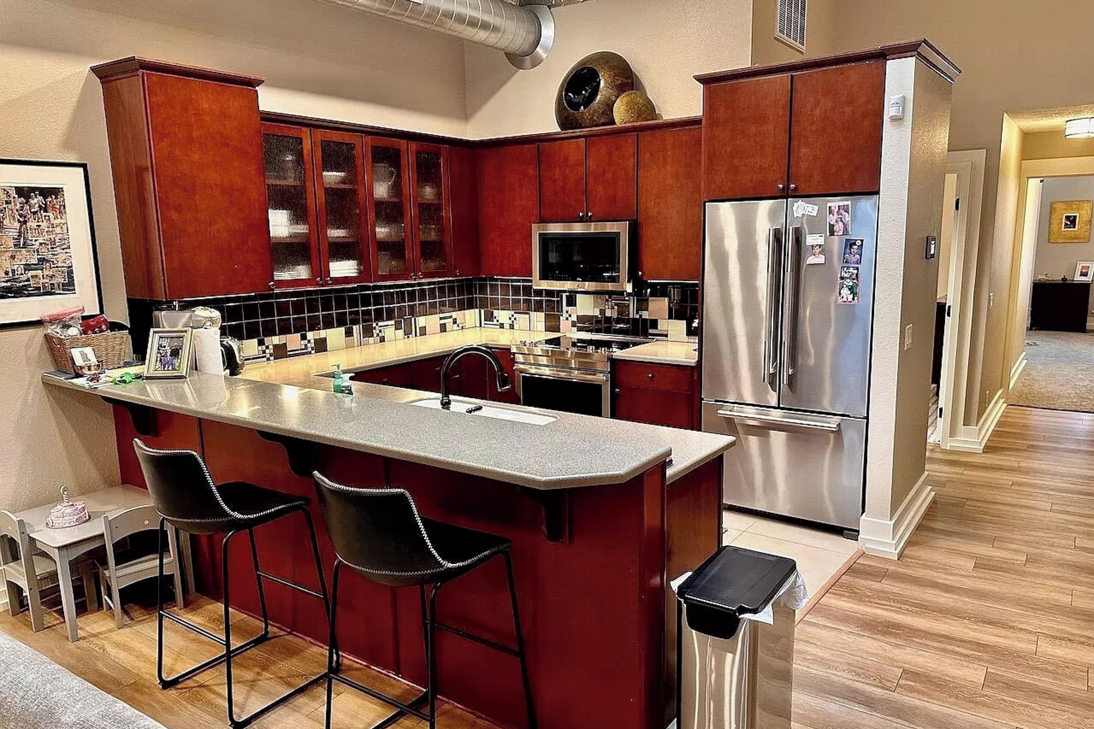 A modern kitchen with dark red cabinets, a stainless steel refrigerator, a microwave, and a large island with bar stools.