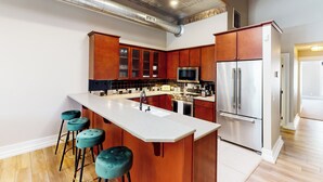 A modern kitchen with wooden cabinets, a stainless steel refrigerator, and a large island with bar stools. - 'downtown Delight' w/ Patio! 1 Mi to Ball State (Muncie)