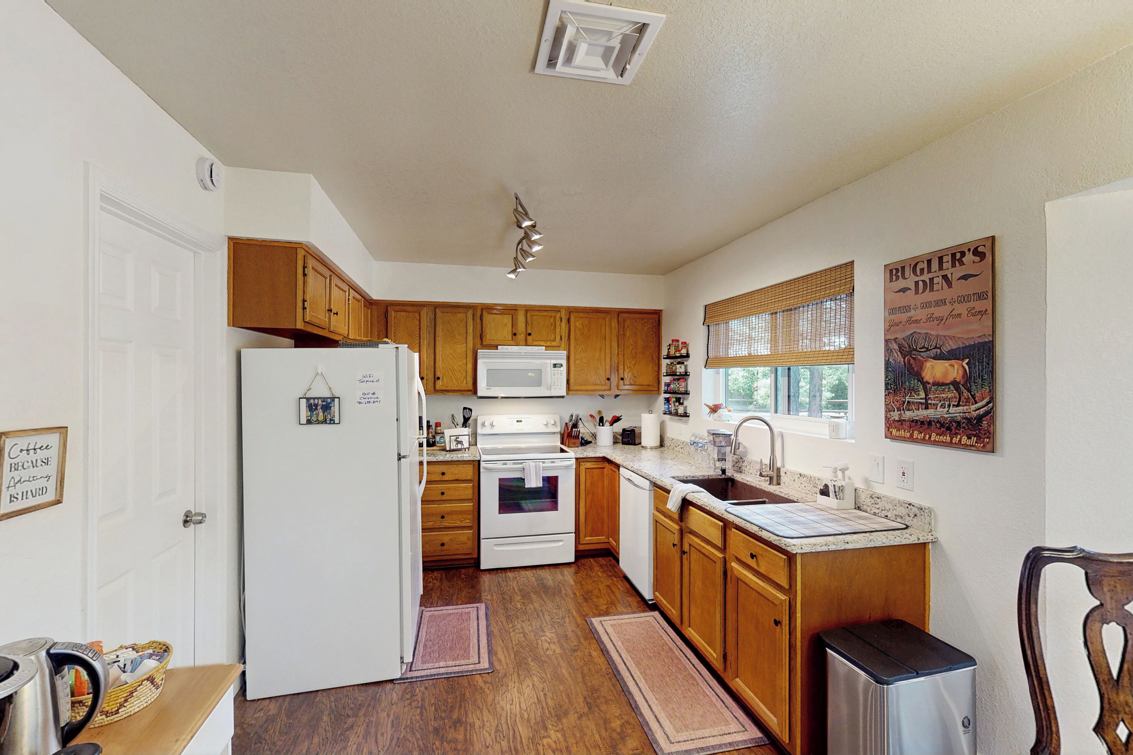 A kitchen with wooden cabinets, a white refrigerator, a stove, and a microwave. There is a window with blinds, a sink, and a chair.