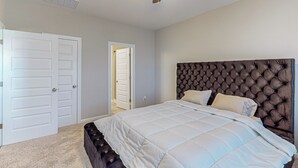Une chambre avec un grand lit, un ventilateur de plafond et deux portes blanches.