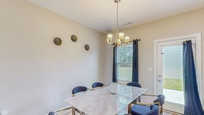 Un espace repas comprenant une table en marbre, six chaises, un lustre et des œuvres d’art décoratives murales.