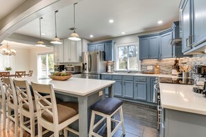 A modern kitchen with white and blue cabinets, stainless steel appliances, and a central island with bar stools. - 4 Seasons of Fun! Walhalla Home w/ Spacious Yard! (Walhalla)