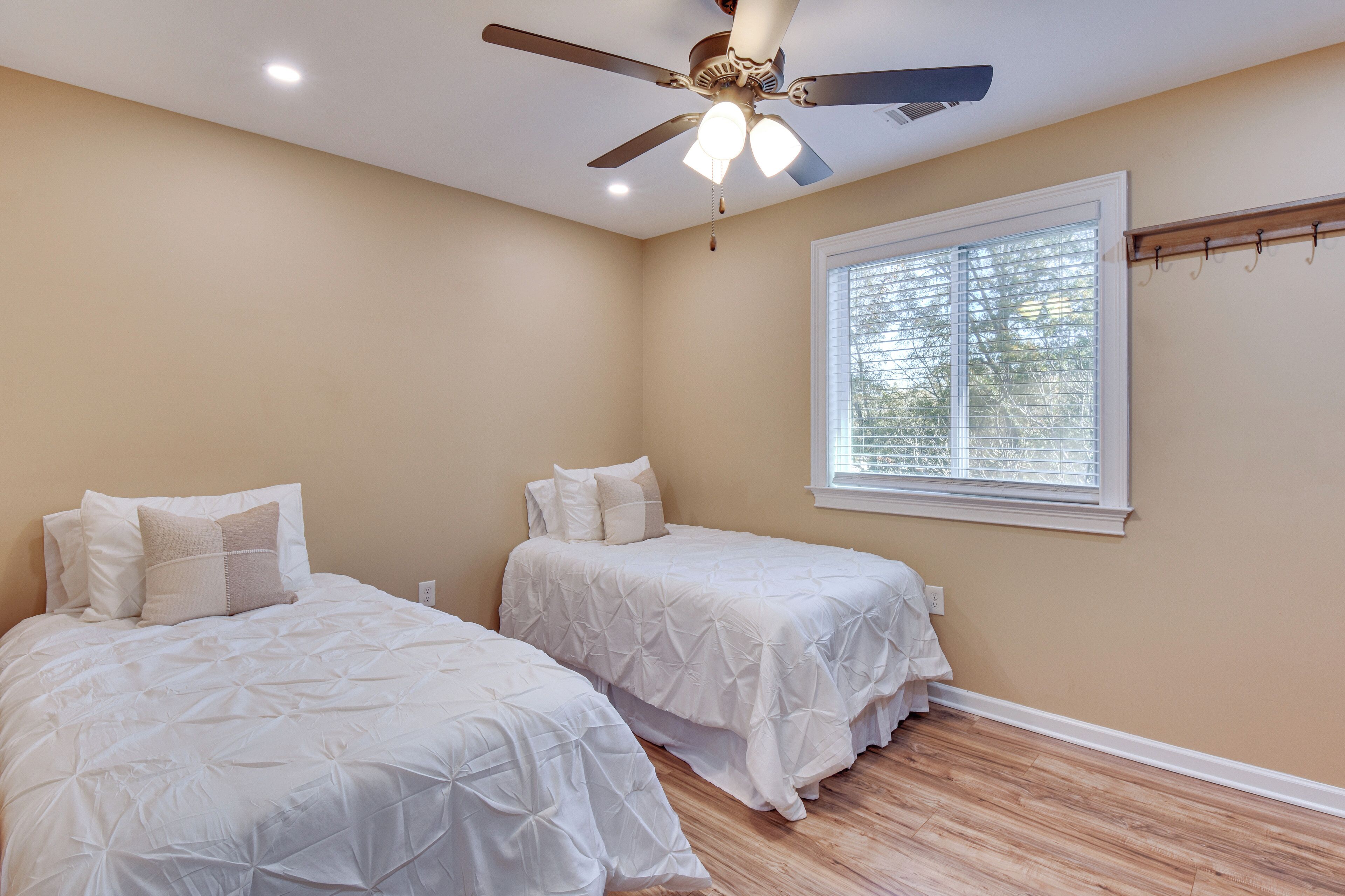 A bedroom with two beds, a ceiling fan, a window with blinds, and a wooden floor.