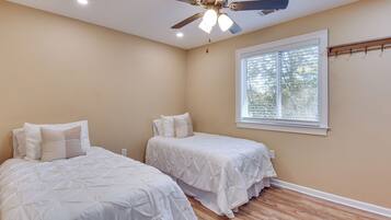 A bedroom with two beds, a ceiling fan, a window with blinds, and a wooden floor.