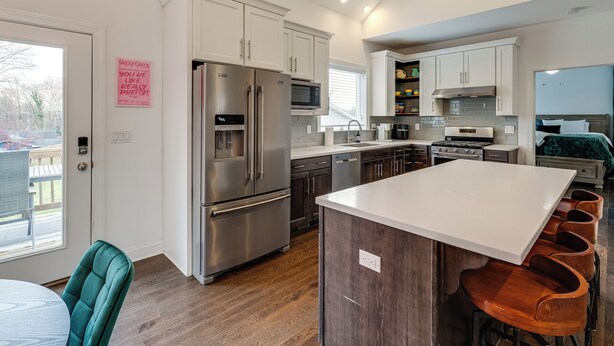 A modern kitchen with stainless steel appliances, white cabinetry, and a central island with bar stools. - Hot Tub & Yard: 'temptation Stays' Home in Roanoke (Roanoke)