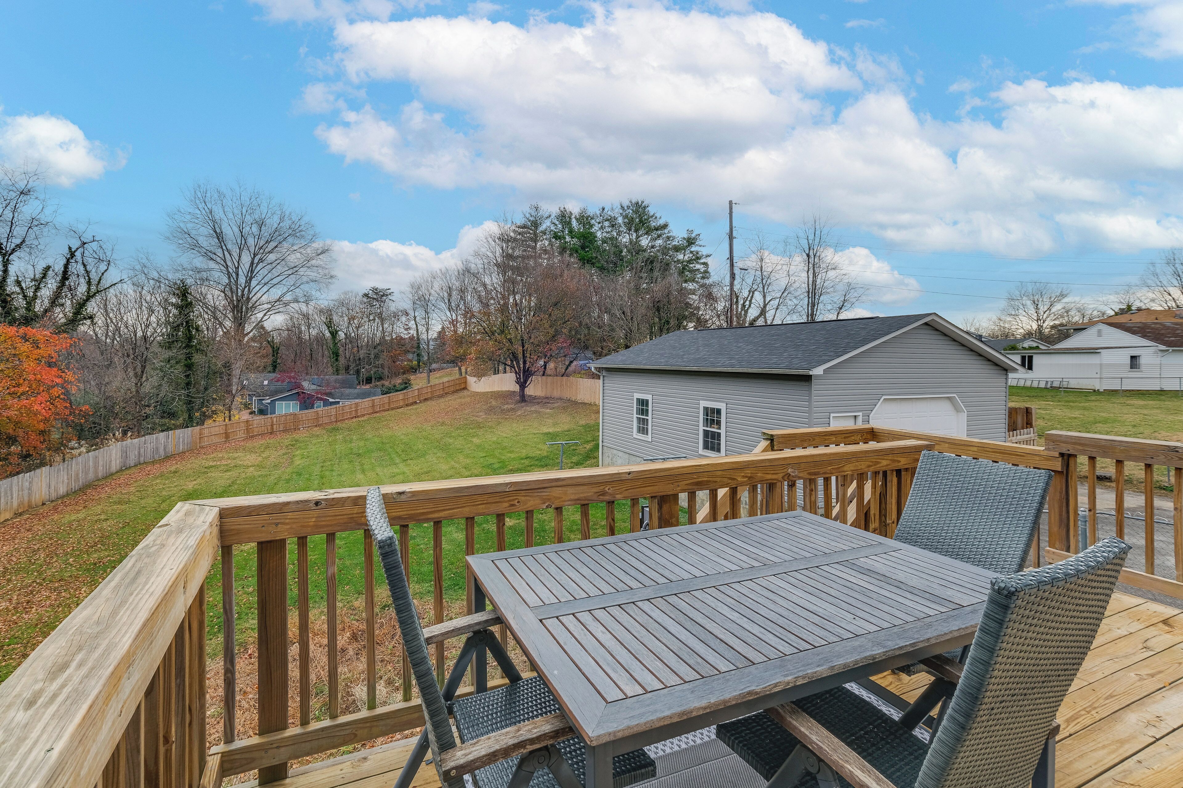 A deck with a table and chairs, a small shed, and a grassy yard with trees and a fence.