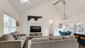 A modern living room with a grey sofa, a flat-screen TV, and a dining area with teal chairs. - Hot Tub & Yard: 'temptation Stays' Home in Roanoke (Roanoke)