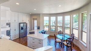 Une cuisine moderne avec des meubles blancs, un îlot central et un coin repas comprenant une table et des chaises en verre.