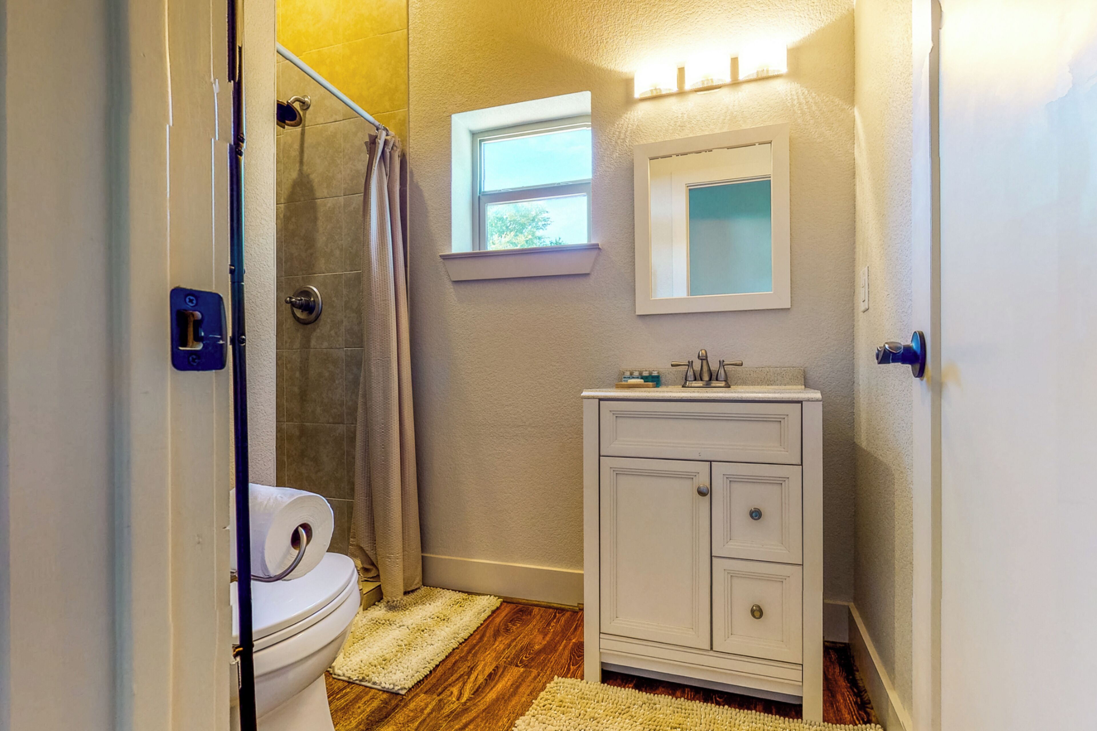 A bathroom with a toilet, a shower, a sink, and a window.
