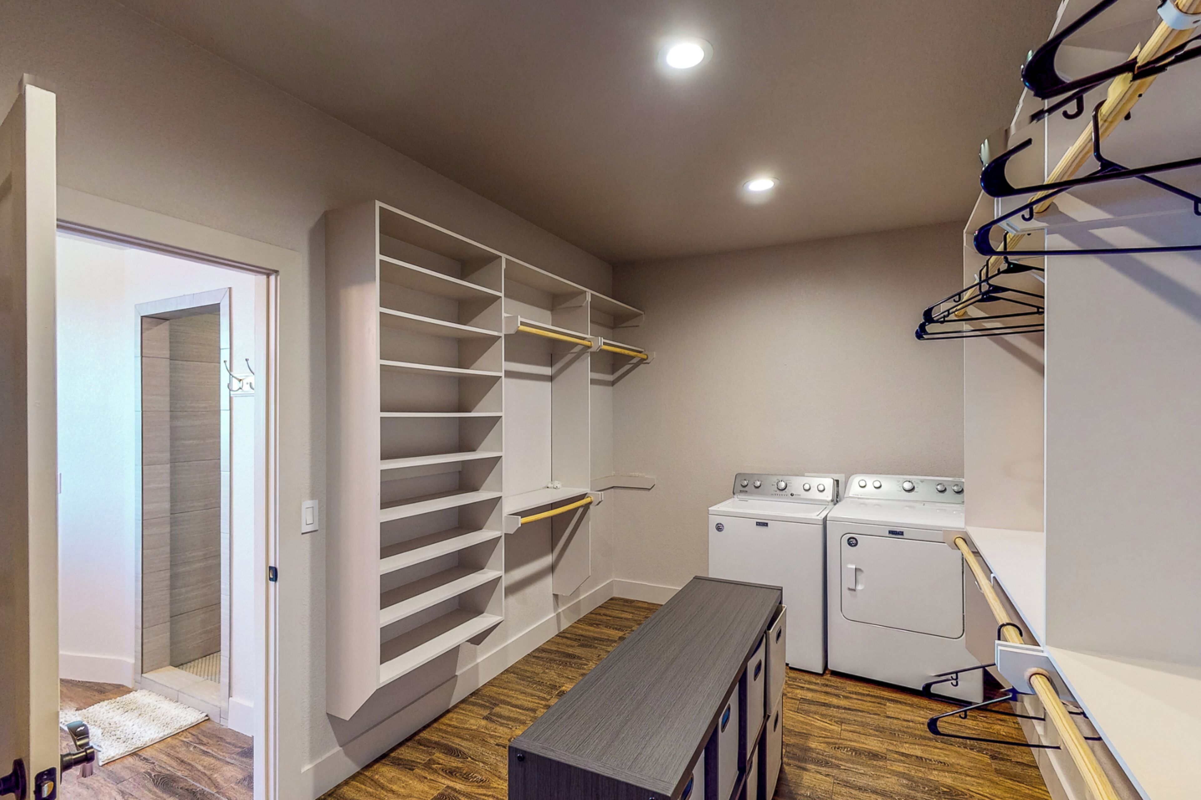 A laundry room with a built-in washer and dryer, a bench, and shelves for storage.