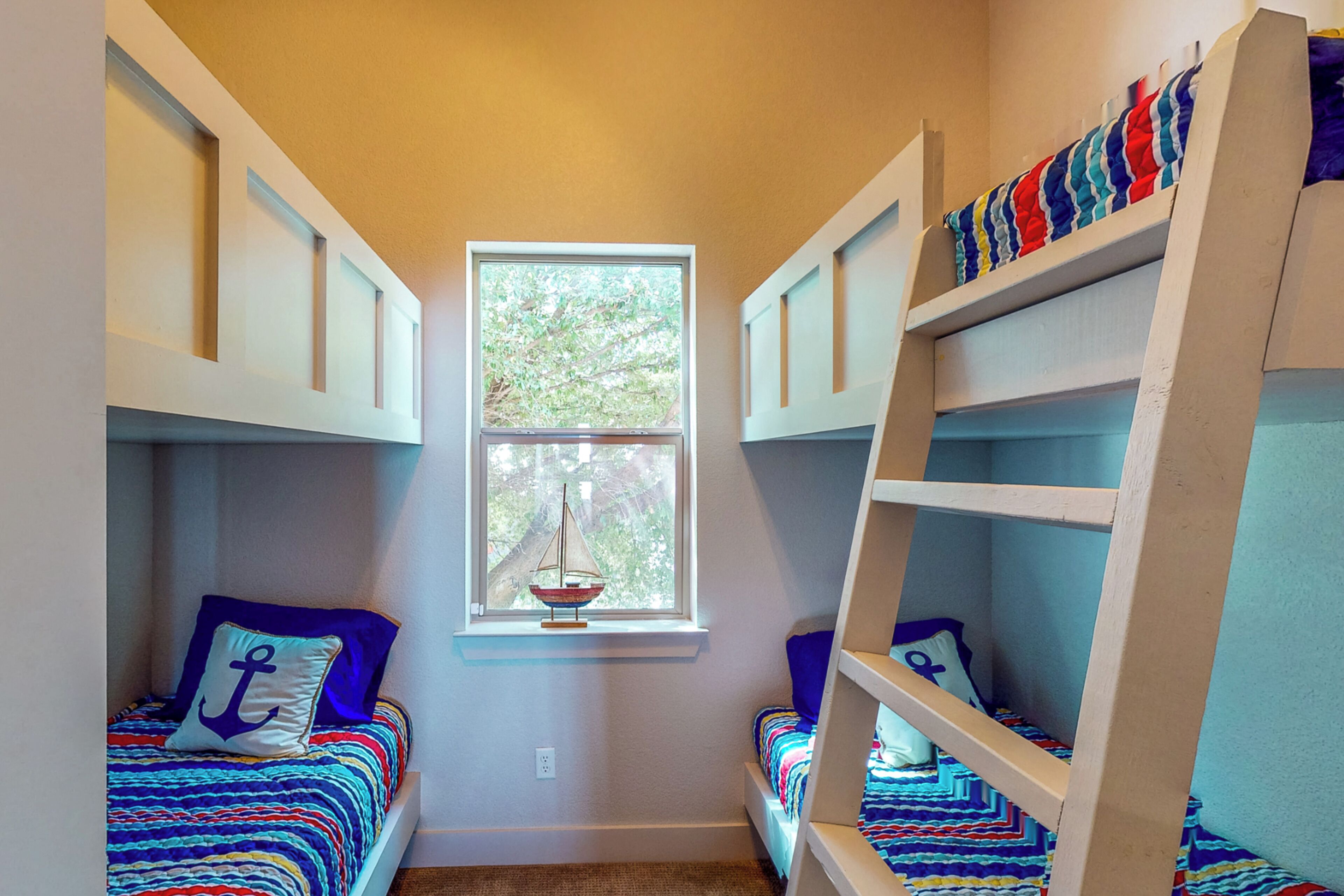 A room with bunk beds, a window with a view of trees, and a small sailboat decoration.