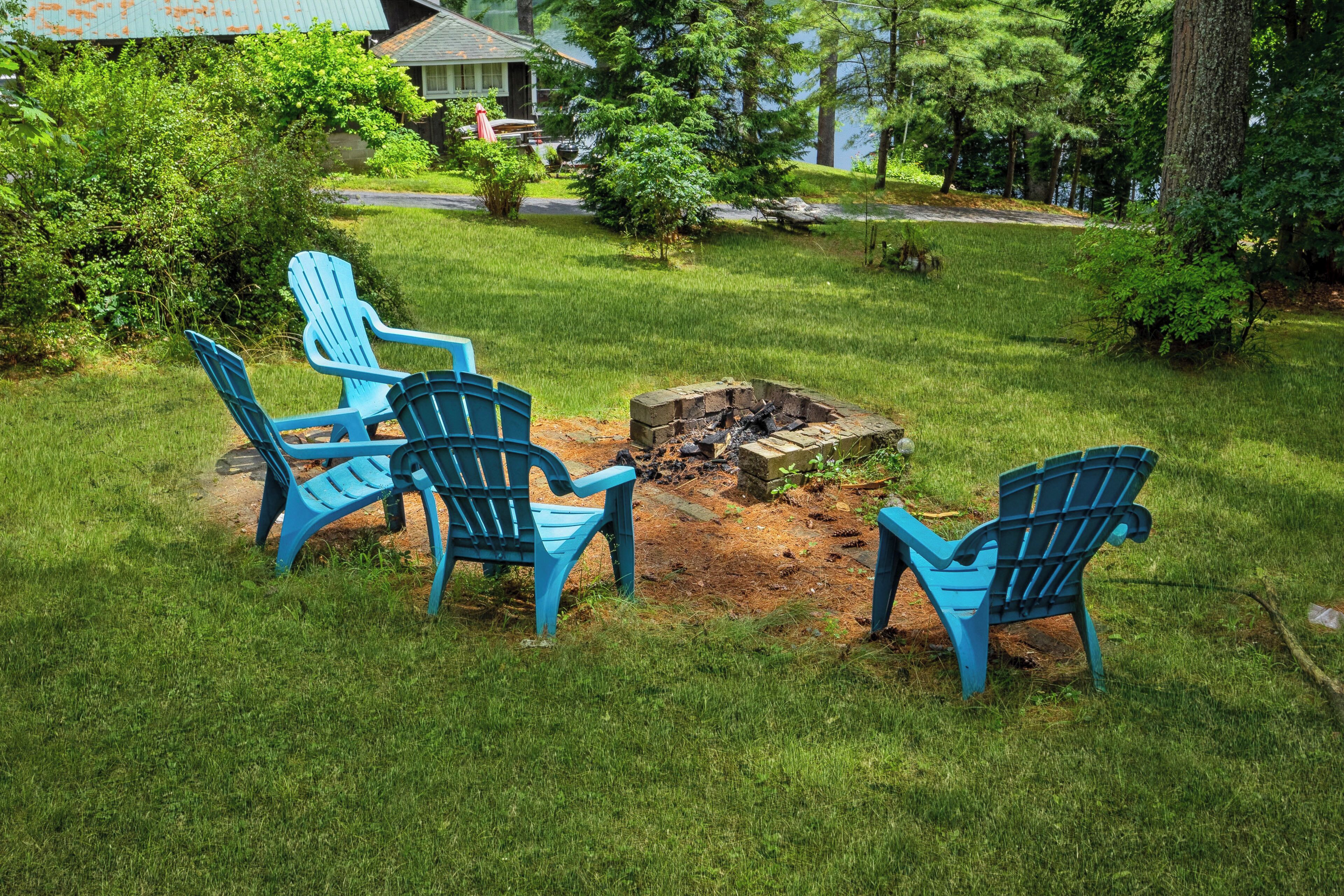 A backyard with a fire pit and four blue Adirondack chairs arranged around it.