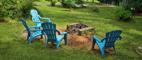 A backyard with a fire pit and four blue Adirondack chairs arranged around it.