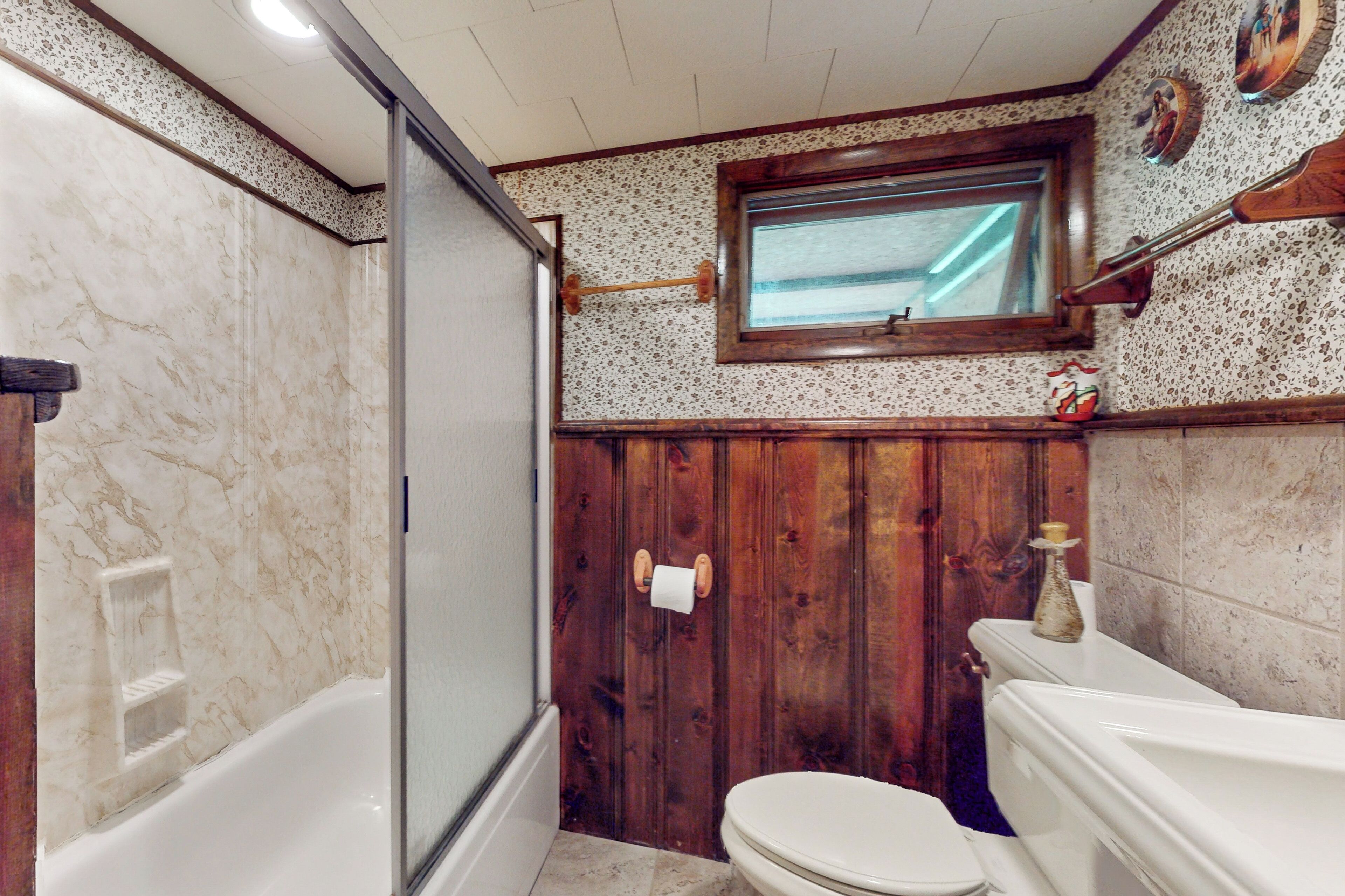A bathroom with a wooden shower enclosure, a toilet, and a bathtub.