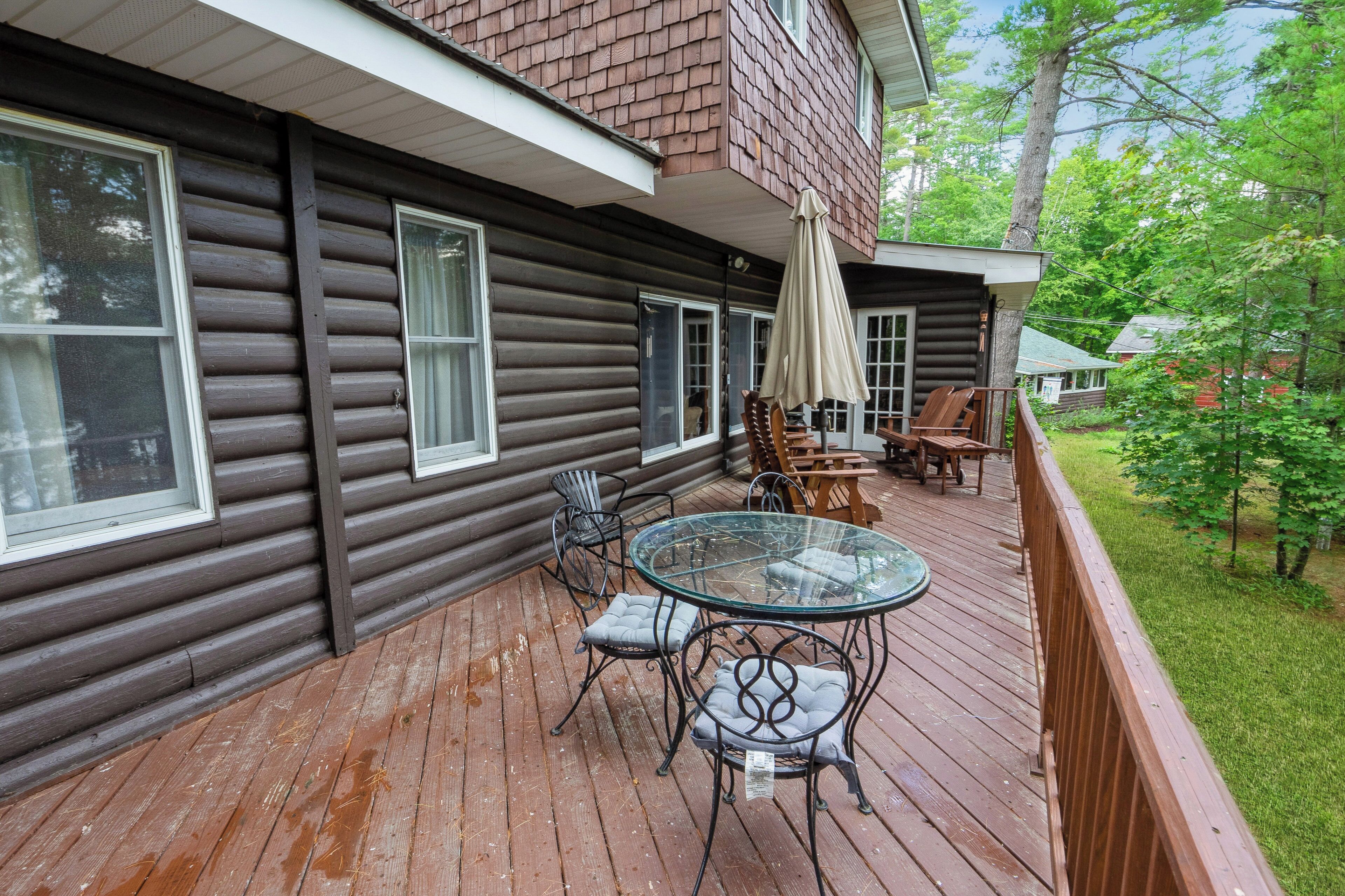 A wooden deck with a glass table and chairs, a covered patio area, and a view of a wooded area.