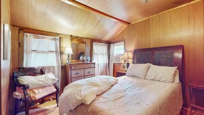 Un dormitorio con una cama grande, paredes de madera, un banco y un aparador.
