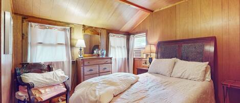 A bedroom with a large bed, wooden walls, a bench, and a dresser.