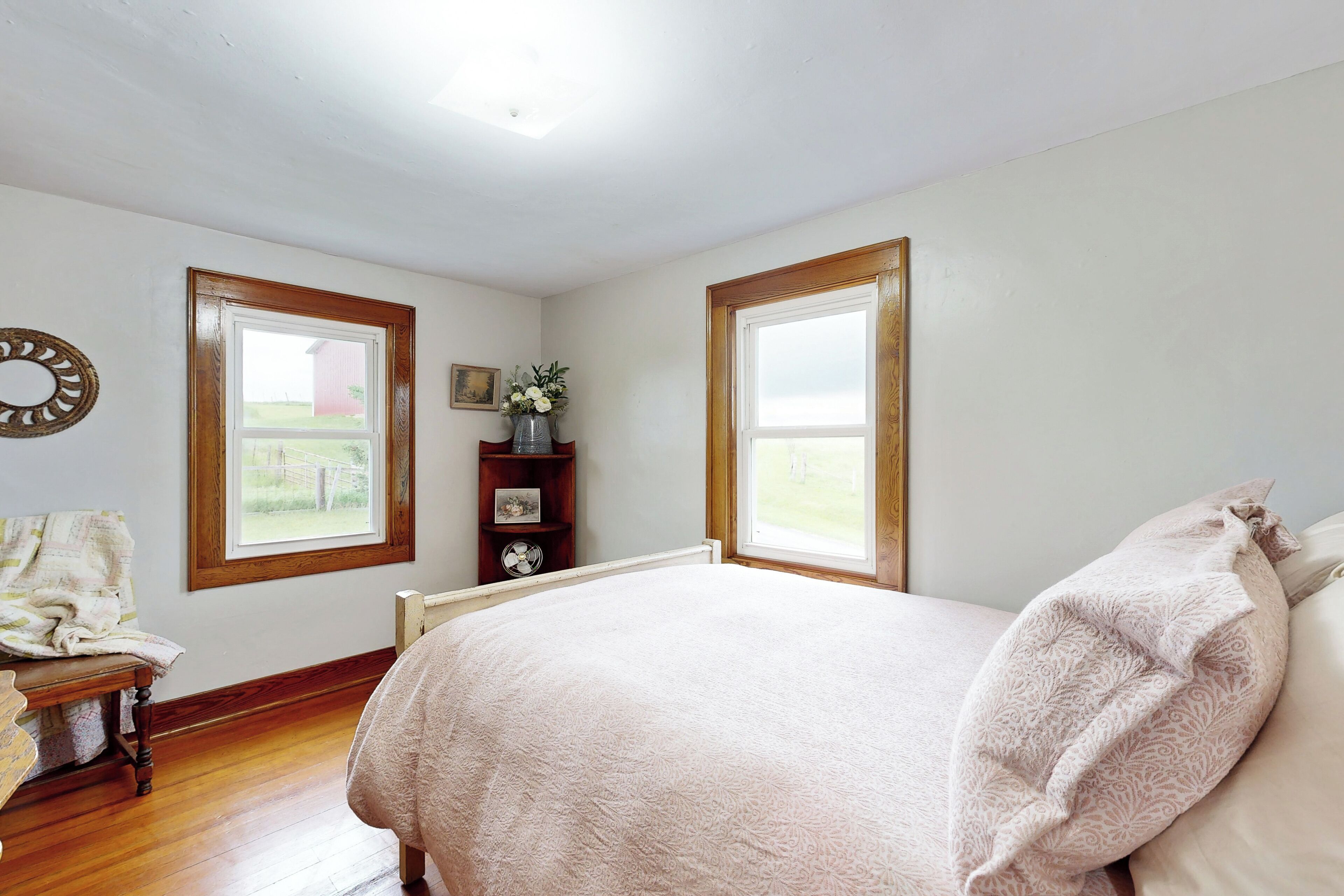 Ein Schlafzimmer mit einem großen Bett, zwei Fenstern, einer Holzkommode und einem Spiegel an der Wand.