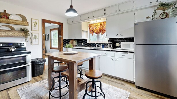 A modern kitchen with white cabinets, a stainless steel refrigerator, a wooden dining table with stools, and a hanging pendant light. - Historic Family Farmhouse w/ Yard in Darlington! (Darlington)