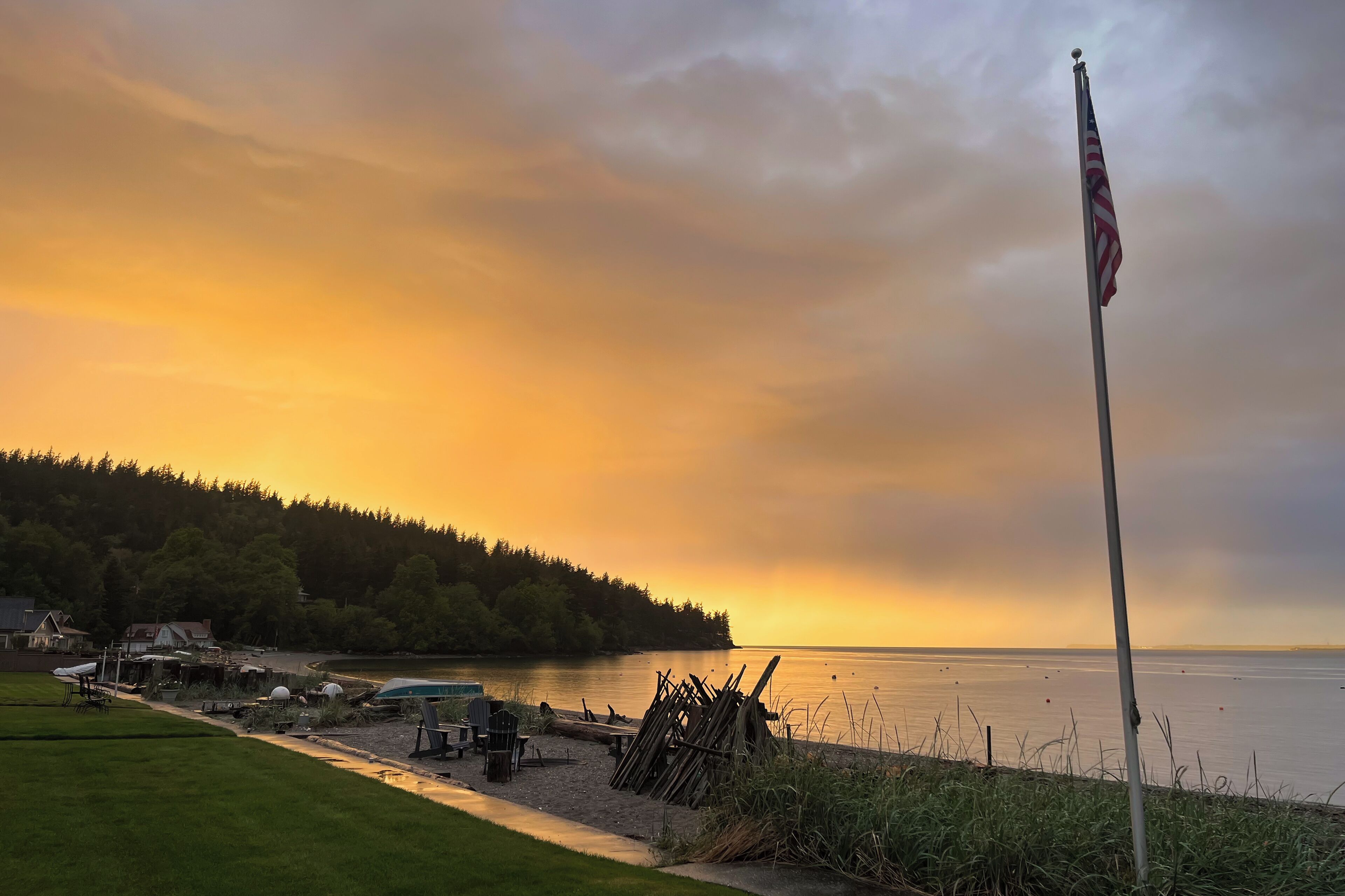 A lakeside scene with a flagpole, boats, and a dock.