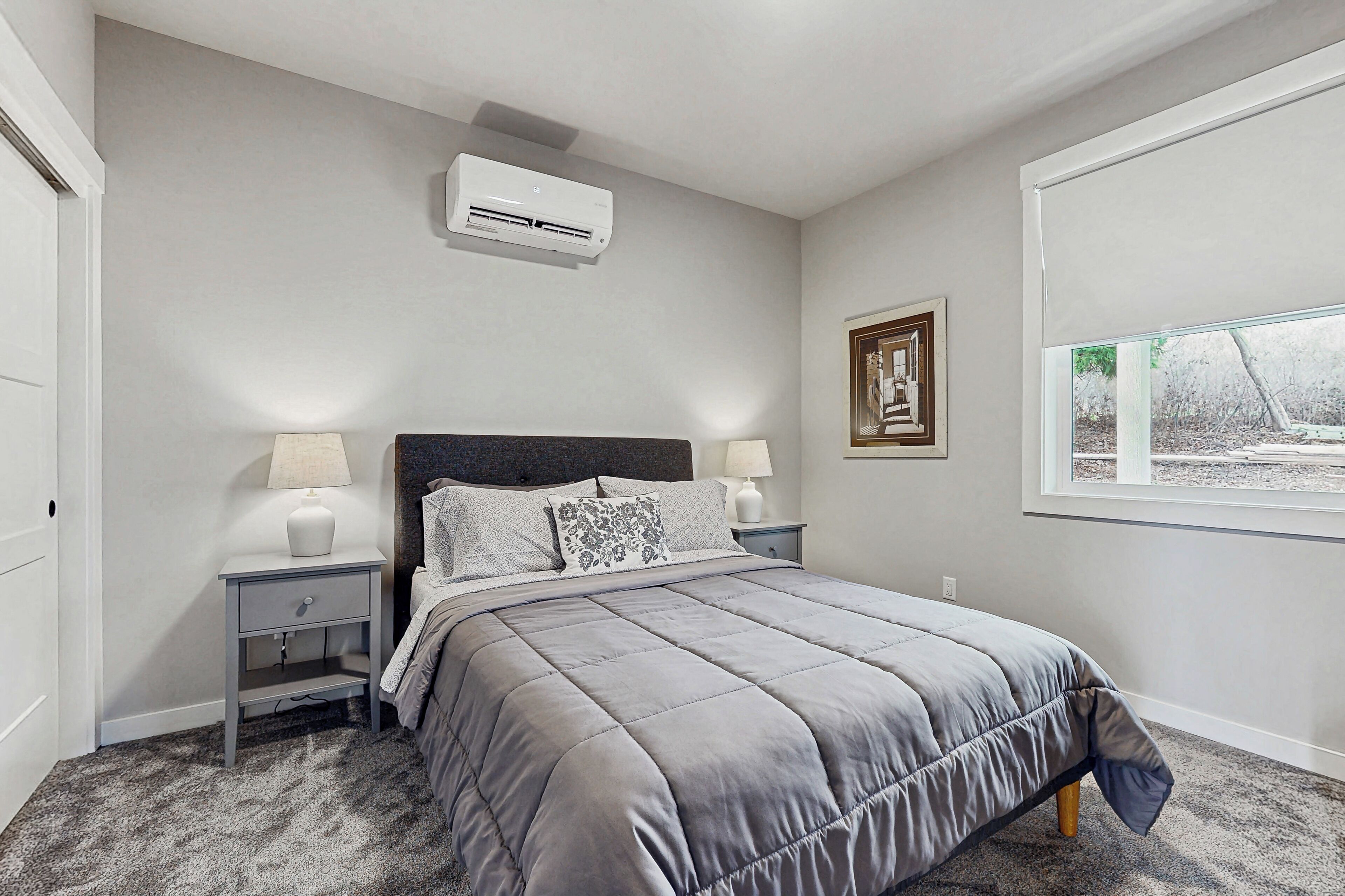 A bedroom with a bed, nightstands, a window, and an air conditioning unit.