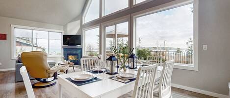 A dining area with a white table set for four, large windows offering a view of the city, and a yellow chair in the foreground.
