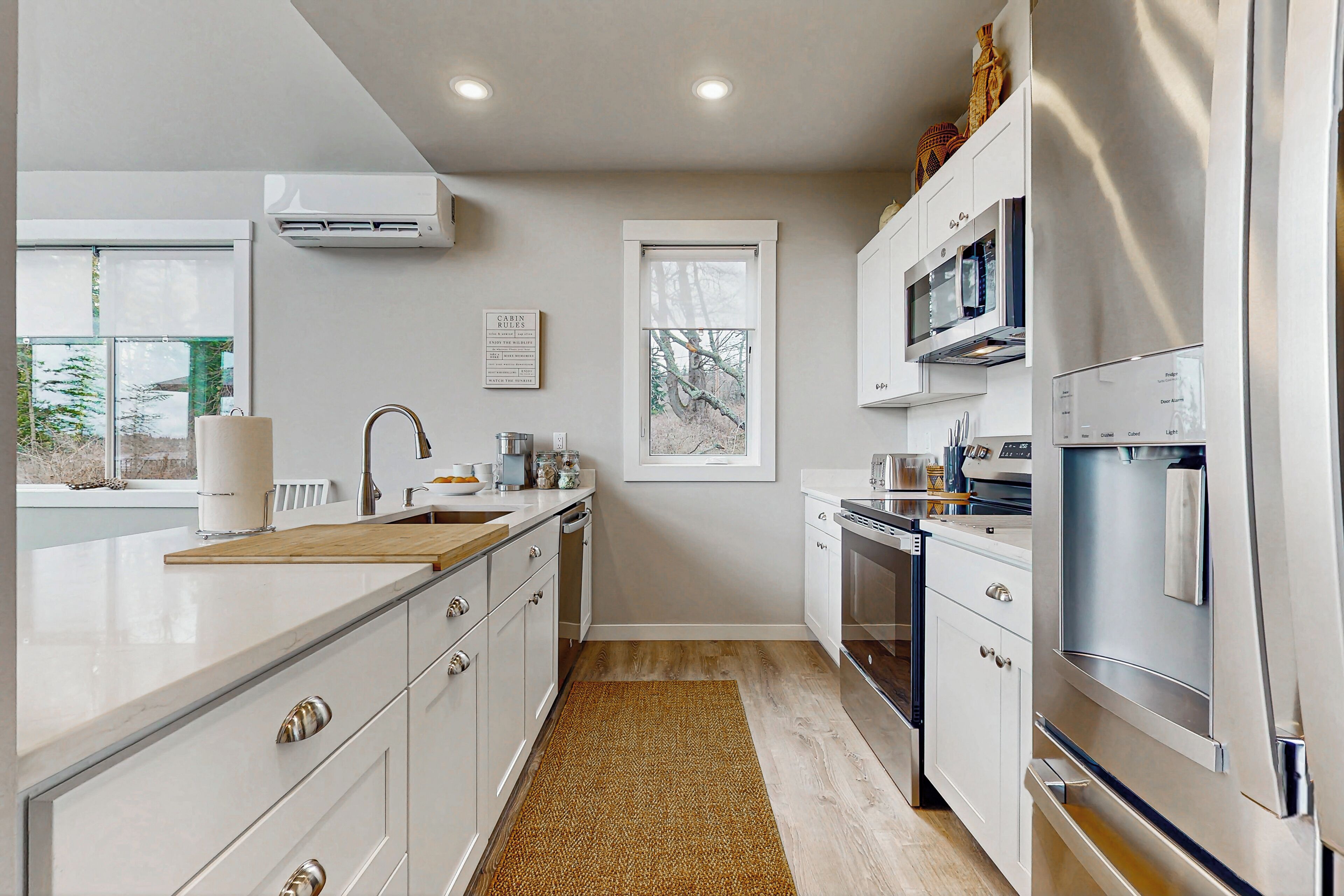A modern kitchen with white cabinetry, stainless steel appliances, and a large window providing natural light.